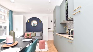 Eine moderne Küche mit grauen Schränken, einer Holzarbeitsplatte und einem Spülbecken. Es gibt einen Essbereich mit einem Tisch für zwei Personen, Stühlen und einem runden Spiegel an der Wand.