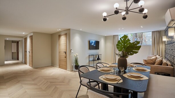Un comedor moderno con suelo de espiga, una mesa central preparada para cuatro personas y una planta grande.