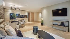 Una sala de estar moderna con sofá, mesa de centro, televisor y una cocina al fondo.