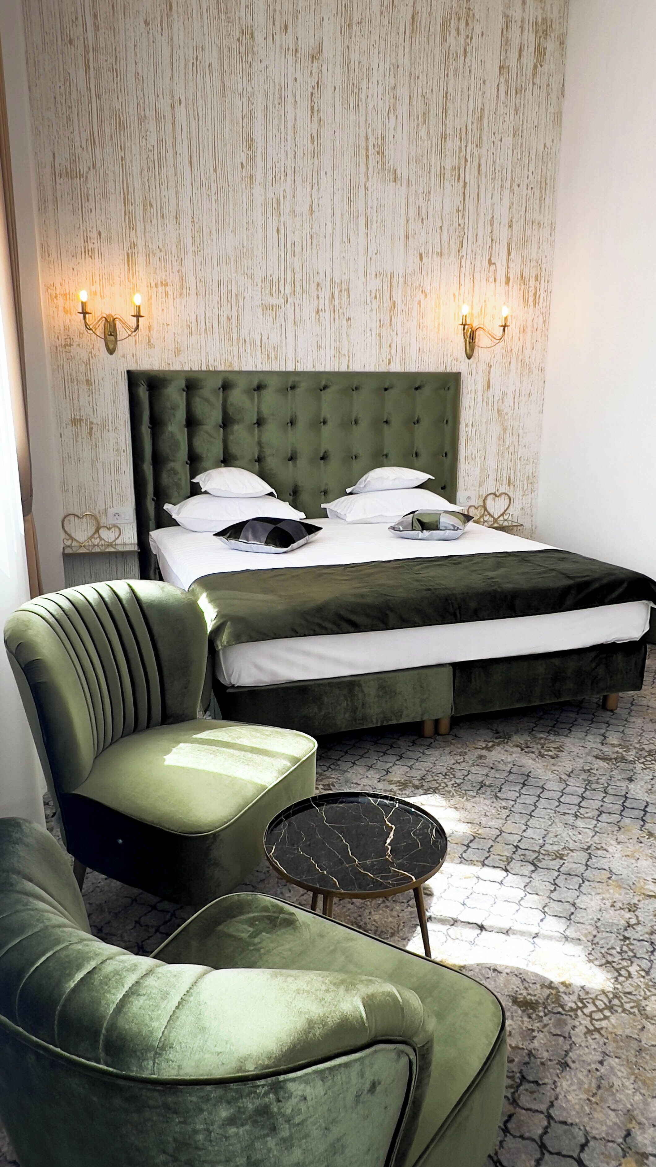 A hotel room with a large bed, two bedside tables, a green armchair, and a patterned floor.