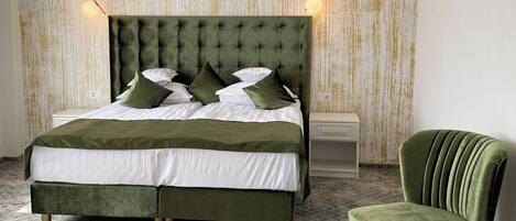 Una cama con cabecera capitonada, una silla tapizada de verde y una pared con diseño.