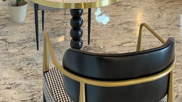 Eine moderne Hotelhalle mit einem runden Marmortisch, schwarzen und goldenen Stühlen, einem violetten Sofa und einer außergewöhnlichen Wandleuchte.