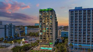 A high-rise hotel with multiple balconies, a swimming pool, and a parking area.