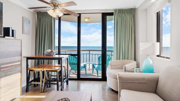 A modern living room with a balcony, a ceiling fan, and a view of the ocean.