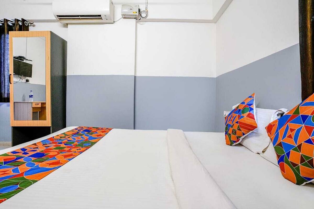 A hotel room with a bed, a mirror, and an air conditioning unit.