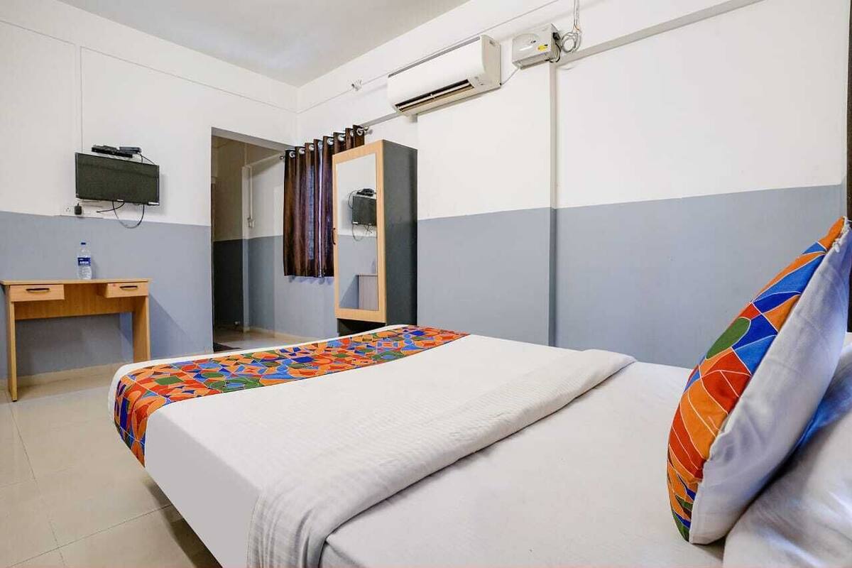 A hotel room with a bed, a desk, a television, and a bathroom visible through an open door.