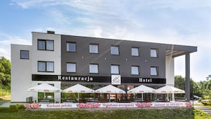 Un moderno edificio de hotel con un letrero que dice "Restauracja Hotel". Hay sombrillas exteriores y un cartel con texto en polaco.