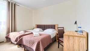 Una habitación de hotel con dos camas, un escritorio de madera, una silla y una mesita de noche.