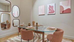 Ein Essbereich mit einem Glastisch, rosa Stühlen und Kunstwerken an der Wand.