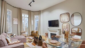 Ein modernes Wohnzimmer mit einem Glastisch, bequemen Sitzmöglichkeiten, einem Kamin und großen Fenstern.