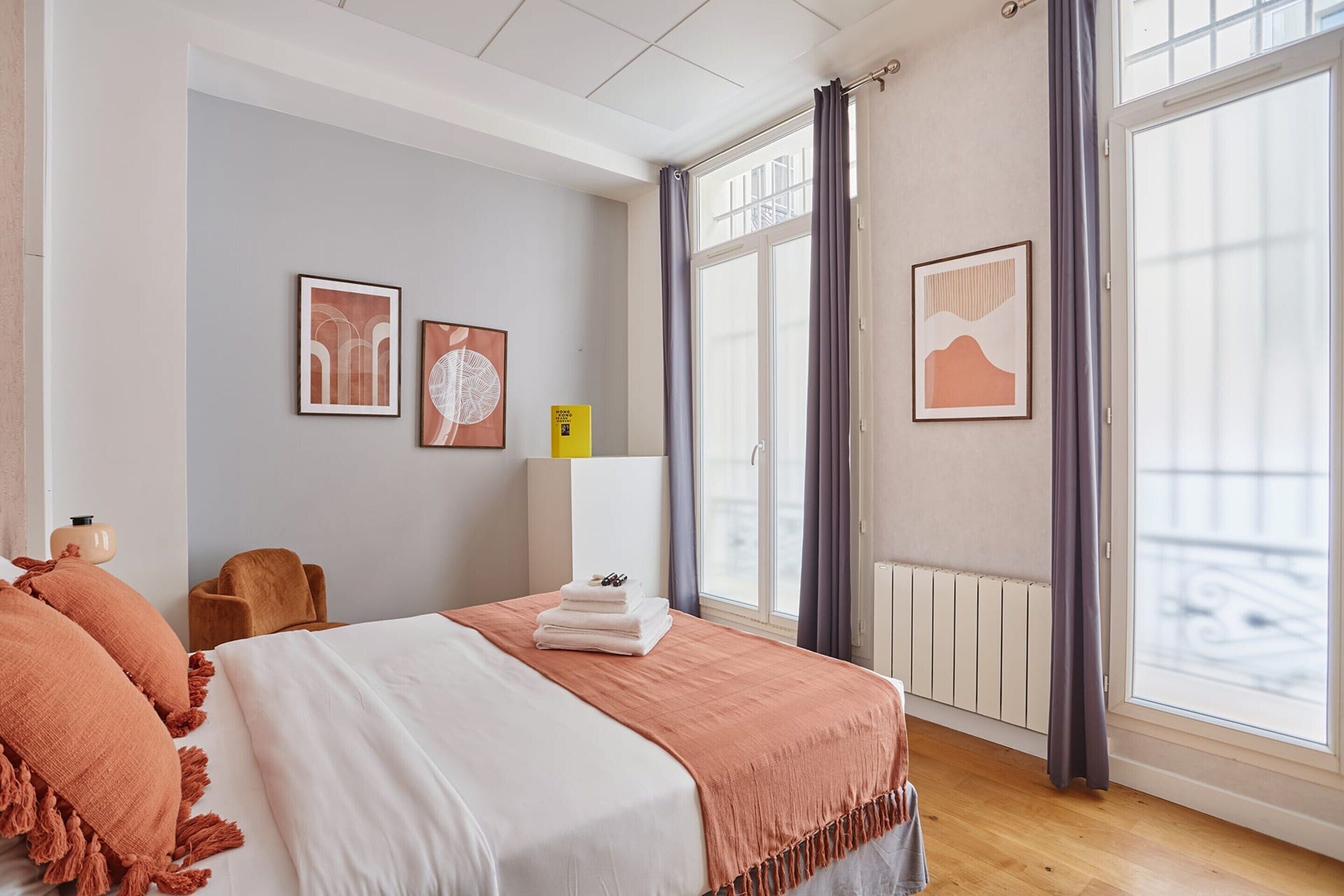 A hotel room with a large bed, a wooden floor, a window with curtains, and artwork on the walls.