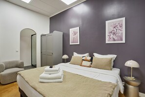 Relax in a serene space with a neatly made bed, comfortable armchair, and natural light pouring in through the large window.