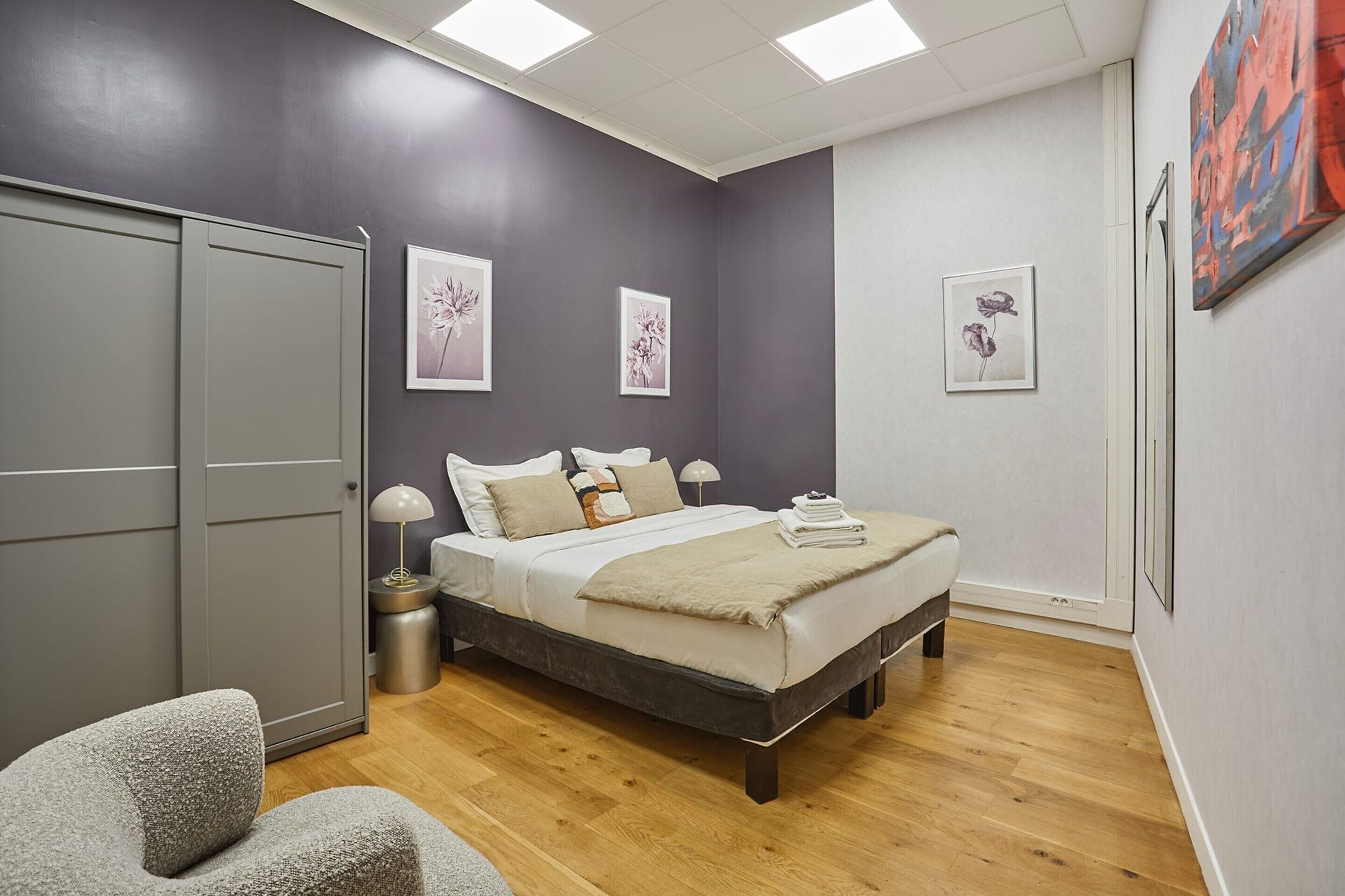 A bedroom with a bed, bedside tables, a wardrobe, and artwork on the walls.