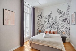 Una camera da letto con un letto grande, una finestra con tende, un murale floreale e una citazione incorniciata al muro.