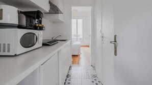 A narrow kitchen with a microwave and coffee maker on the counter, a door leading to a living area, and patterned floor tiles. - Lovely Studio for 2 People - Levallois-perret (Levallois-Perret)