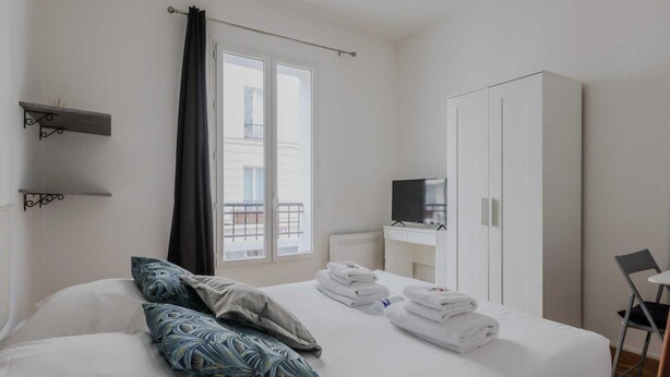 A hotel room with a bed, a TV, a wardrobe, and a window with curtains. - Lovely Studio for 2 People - Levallois-perret (Levallois-Perret)