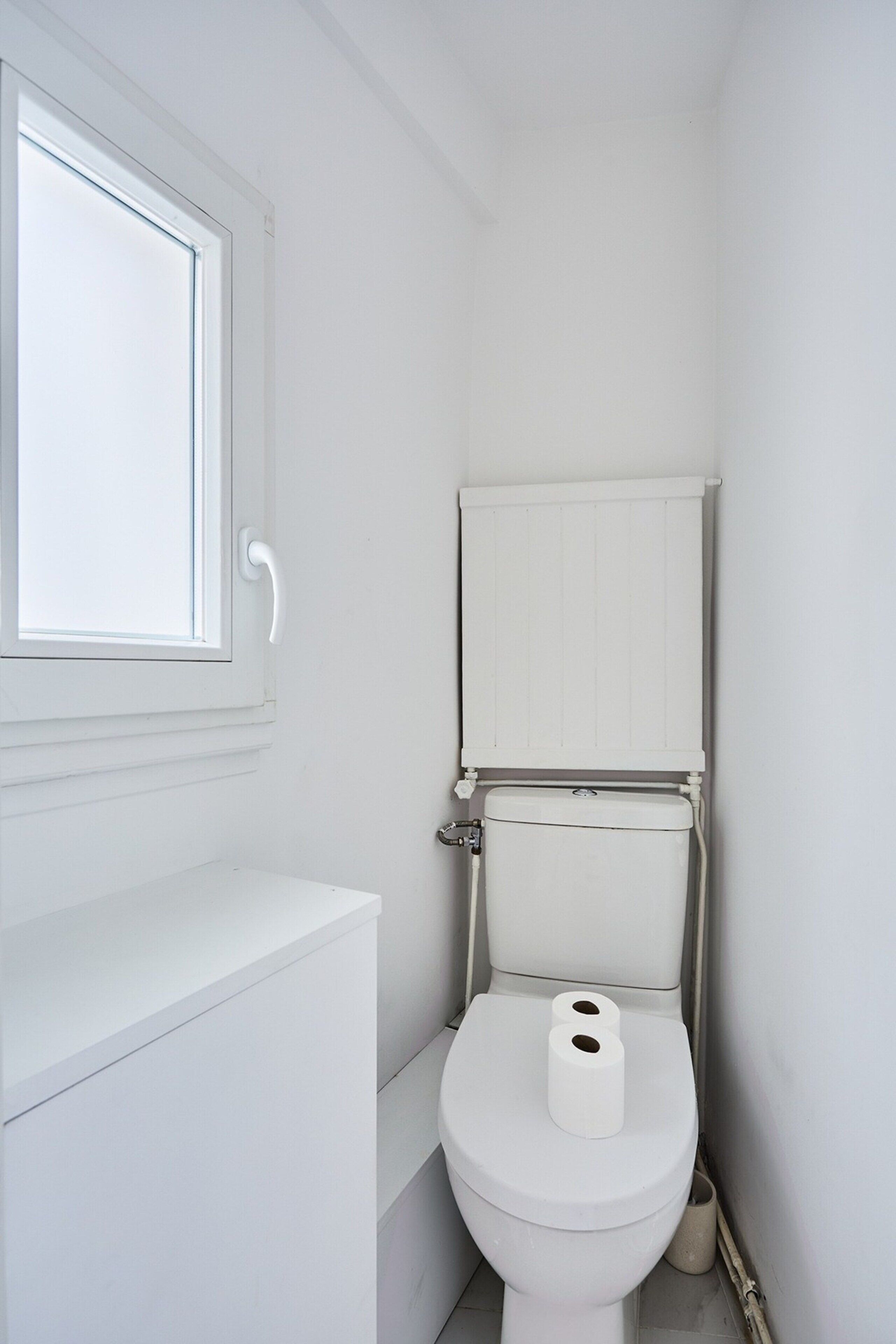 A small, white bathroom with a toilet, a window, and a radiator.