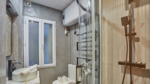 A modern bathroom with a glass shower enclosure, a toilet, and a sink with a towel and toilet paper. - Charming Apartment Louvre Museum (Paris)