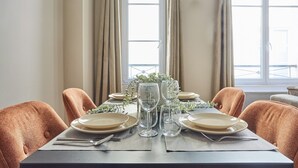 A dining table set with plates, glasses, and cutlery, flanked by chairs, with a window and curtains in the background. - Charming Apartment Louvre Museum (Paris)