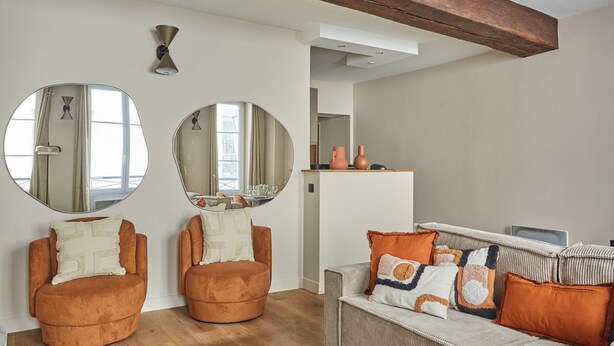 A living room with two round armchairs, a sofa, and a coffee table. There are two large mirrors on the wall, a ceiling light, and a wooden beam above the sofa. - Charming Apartment Louvre Museum (Paris)