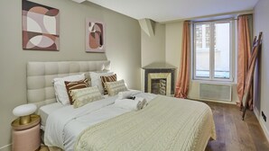 A bedroom with a large bed, a fireplace, and artwork on the wall. - Charming Apartment Louvre Museum (Paris)