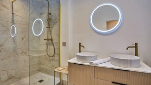 Un bagno moderno con doccia vetrata, due lavabi con specchi circolari e pavimento in marmo.