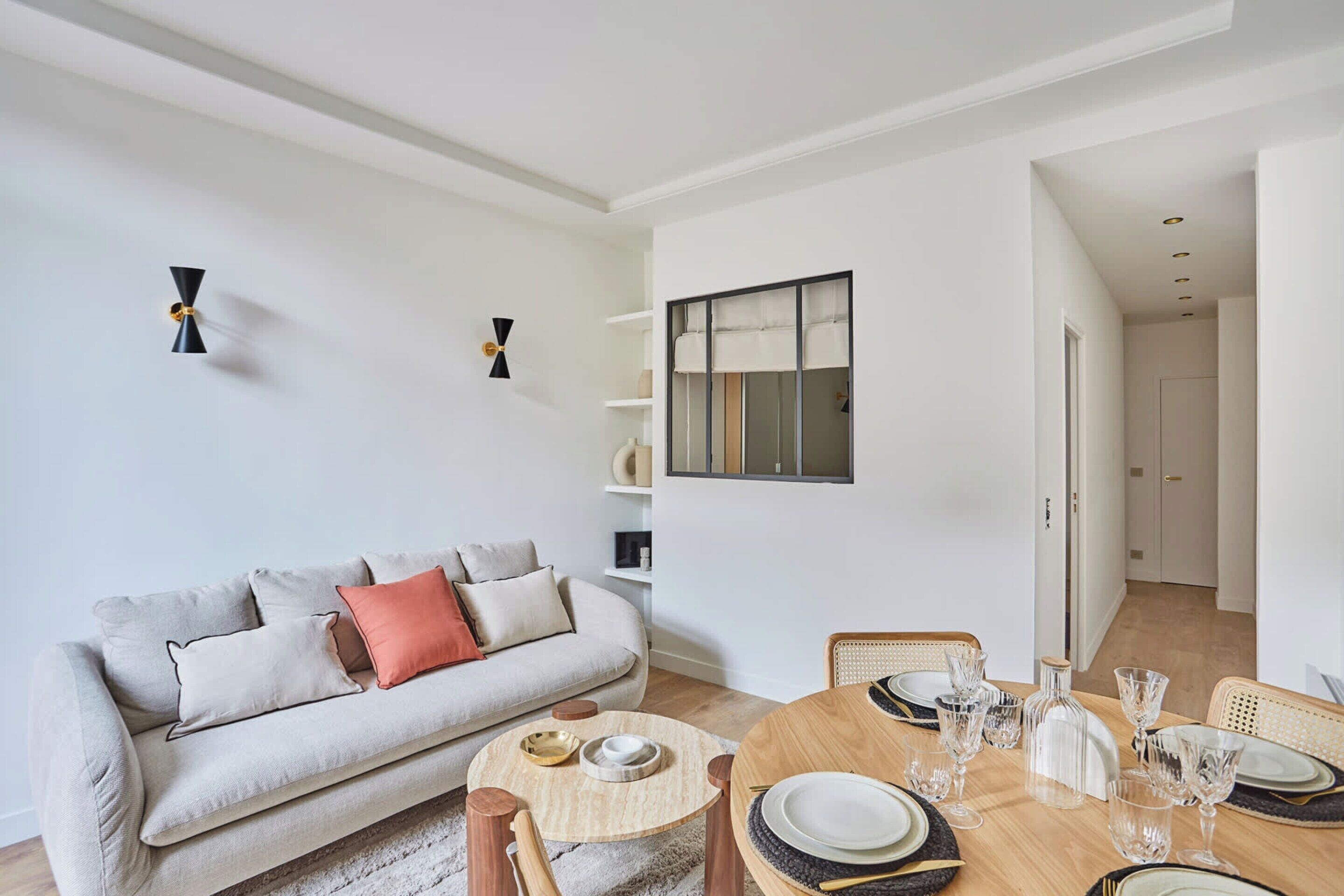 A modern living room with a sofa, a dining table set for four, and a bookshelf.