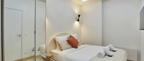 A modern bedroom with a bed, bedside tables, a nightstand, a mirror, and a ceiling light fixture.