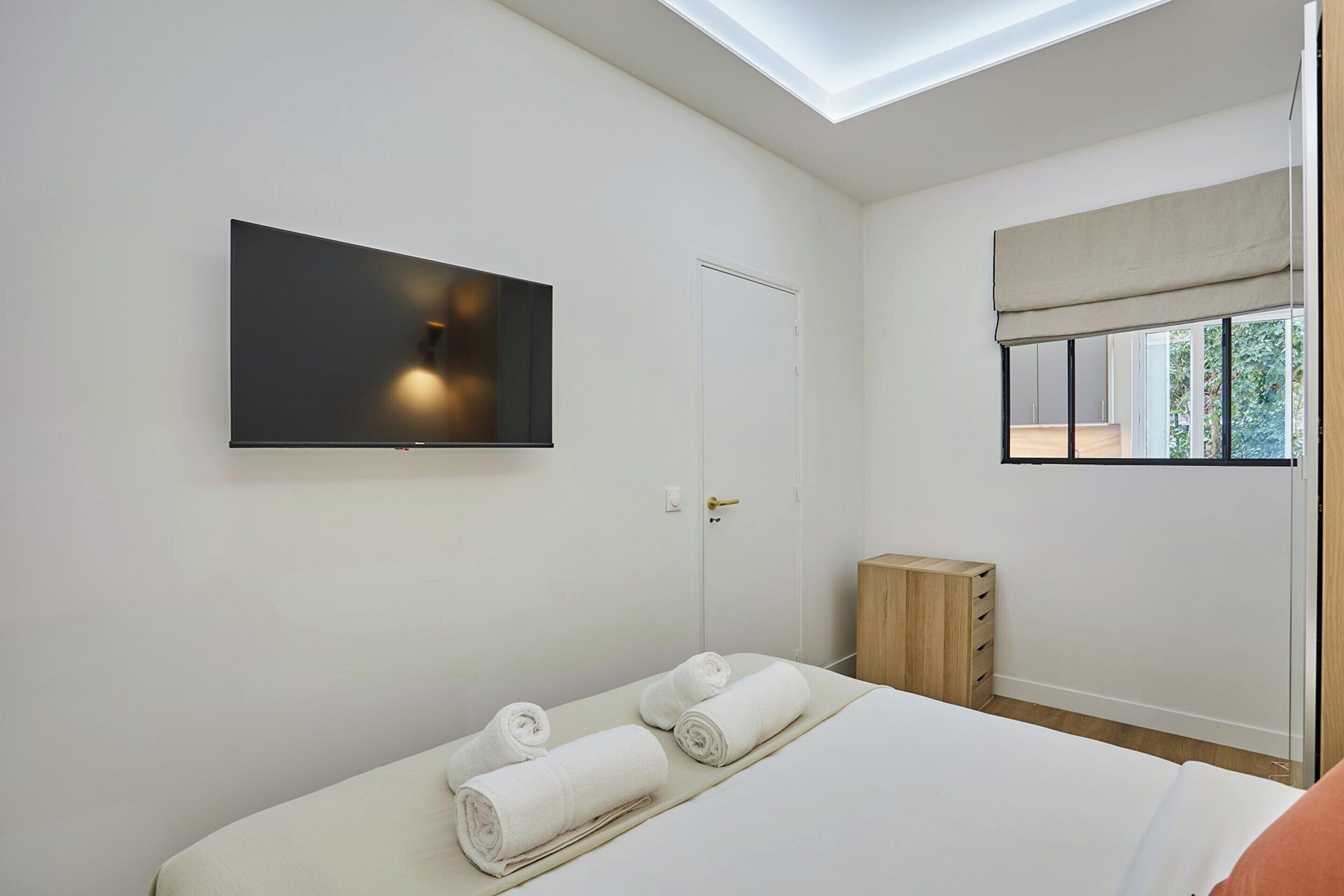 Une chambre à coucher comprenant un lit, un téléviseur à écran plat fixé au mur, une fenêtre avec vue et un puits de lumière.