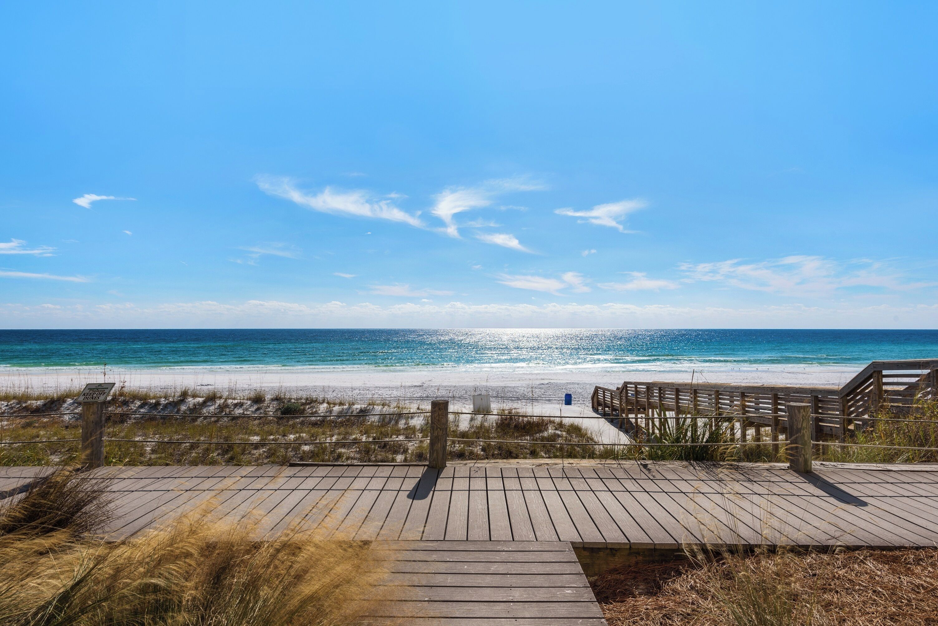 A wooden boardwalk leading to a beach with clear skies and calm waters.