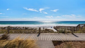 A wooden boardwalk leading to a beach with clear skies and calm waters.