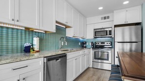 A modern kitchen with white cabinets, stainless steel appliances, and a blue tiled backsplash.