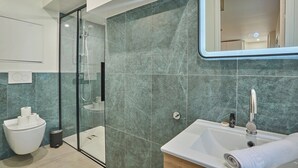 A modern bathroom with a glass shower enclosure, a white sink, and a marble-tiled wall. - Amazing Studio Le Marais (Paris)
