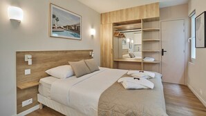 A modern bedroom with a wooden headboard, a large bed with white bedding, a bedside table, a built-in wardrobe, and a framed picture on the wall. - Amazing Studio Le Marais (Paris)