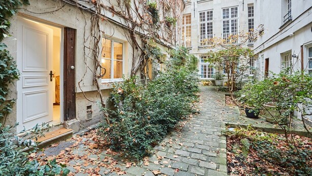 A narrow cobblestone alleyway with a building on one side and a tree-lined path on the other. - Amazing Studio Le Marais (Paris)