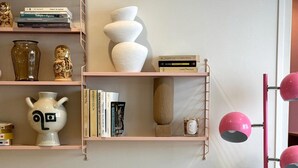 En stue med sofa, lyserød lampe og reoler med bøger og pynteting.