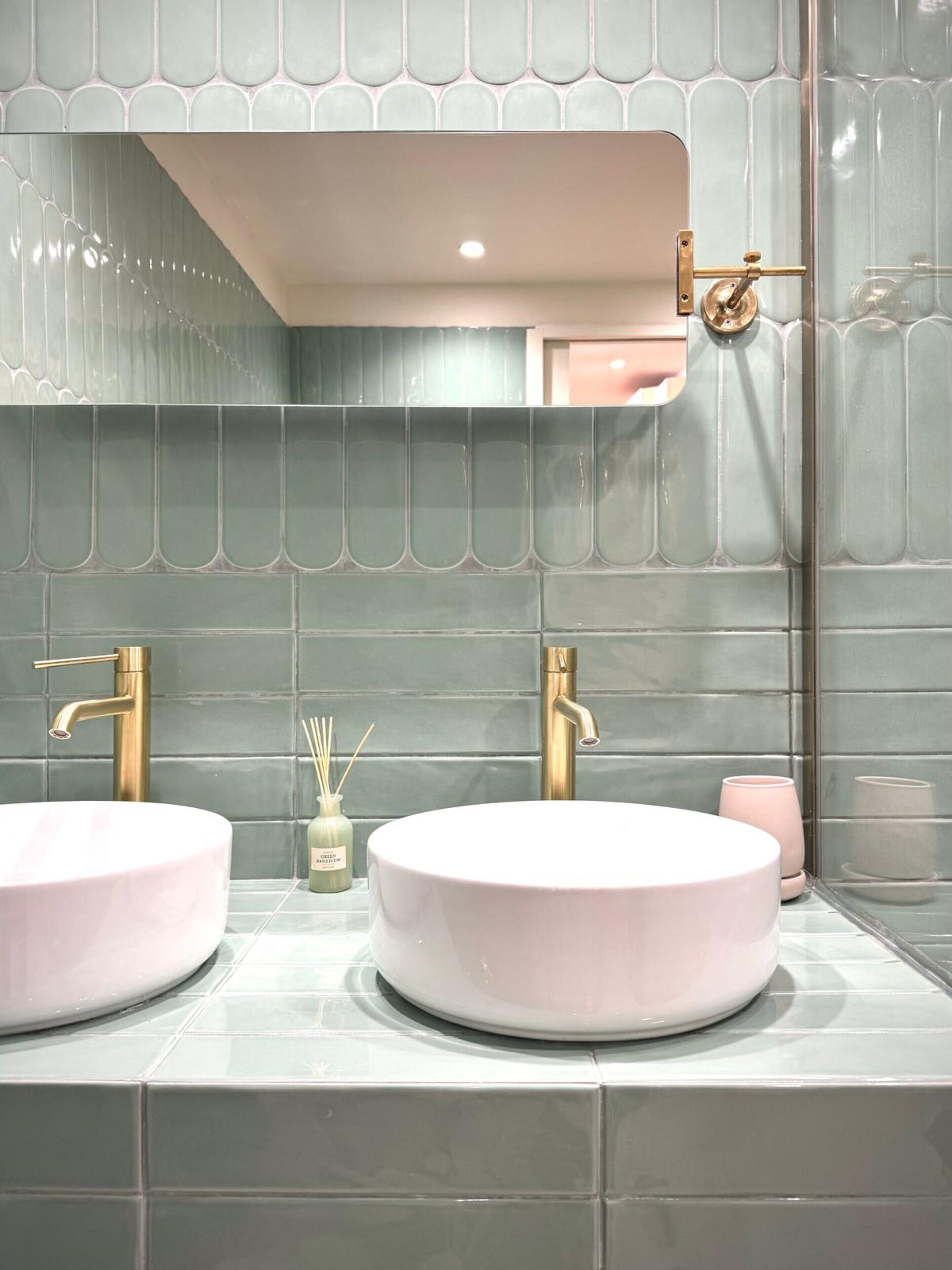 A bathroom with two round sinks, a mirror, and a towel rack.