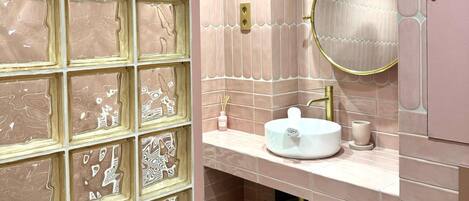 Un baño con pared de azulejos, un lavabo, un espejo y una cesta.