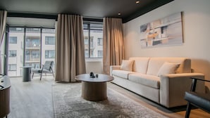 Una sala moderna con un sofá, una mesa de centro y vistas de un edificio a través de grandes ventanales.