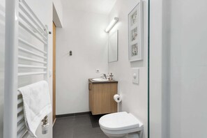 A modern bathroom with a toilet, sink, and towel rack. - Blue Mountain Apartments - Family Studio (Kópavogur)