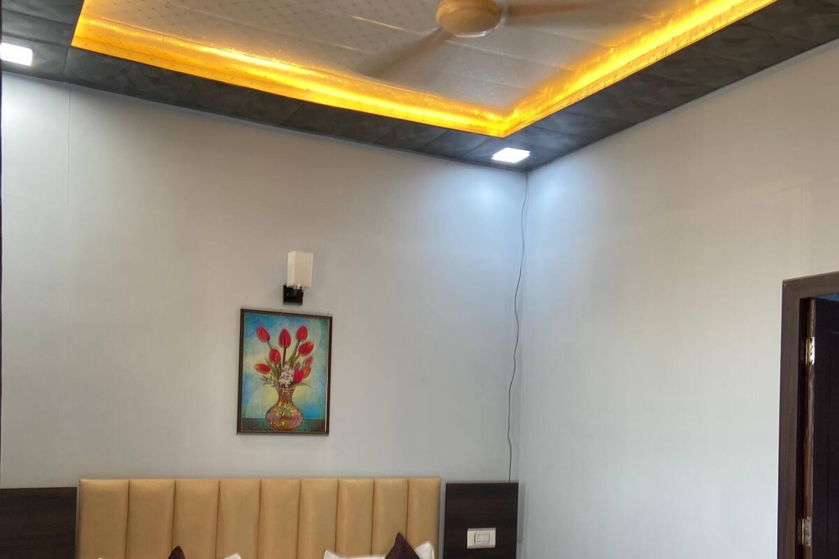 Habitación de hotel con una cama grande, ventilador de techo, lámpara de pared y un cuadro de flores.