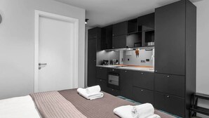 A modern hotel room with a bed, two towels, a kitchenette, and a white door. - Backyard Stylish Studio for 4 - Excellent Location (Reykjavík)