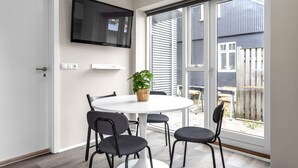 A modern room with a round table, four chairs, a flat-screen TV mounted on the wall, and a sliding glass door leading to an outdoor area. - Freyjugata Apartments - Central Studio (Reykjavík)