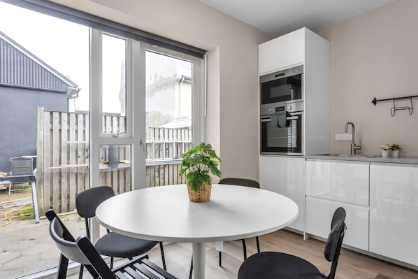 Une cuisine moderne avec des armoires blanches, un four encastré et une fenêtre donnant sur un jardin.