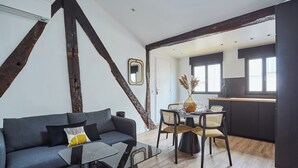 A modern living room with a sofa, coffee table, and dining area with chairs. - Apartment AC 2 Bedrooms Le Marais Beaubourg (Paris)