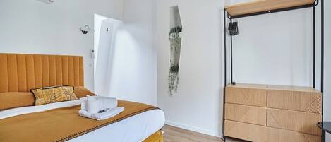 Habitación de hotel con una cama grande, cabecera de madera, un banco integrado y una planta en la pared.