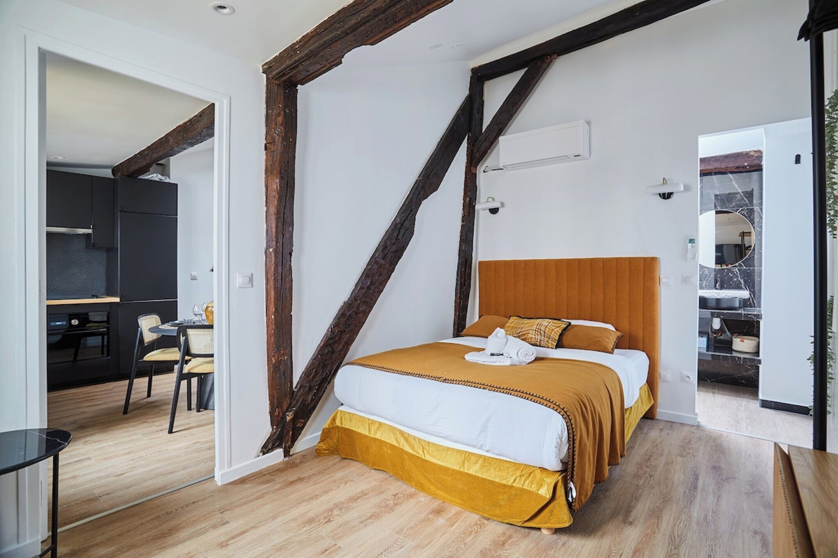 A bedroom with a wooden headboard, a bed with a white and mustard-colored bedding, and a small table with chairs.
