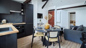A modern kitchen with dark cabinetry, a wooden dining table, and a sofa in a living area. - Apartment AC 2 Bedrooms Le Marais Beaubourg (Paris)