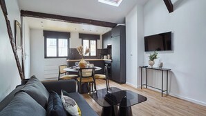 A modern living room with a sofa, a glass coffee table, and a dining area with chairs and a table. - Apartment AC 2 Bedrooms Le Marais Beaubourg (Paris)