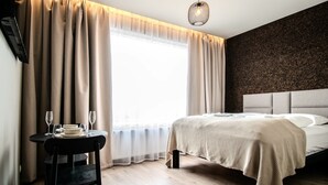Un dormitorio moderno con una cama grande, una mesita de noche con vasos y vistas al exterior a través de cortinas translúcidas.
